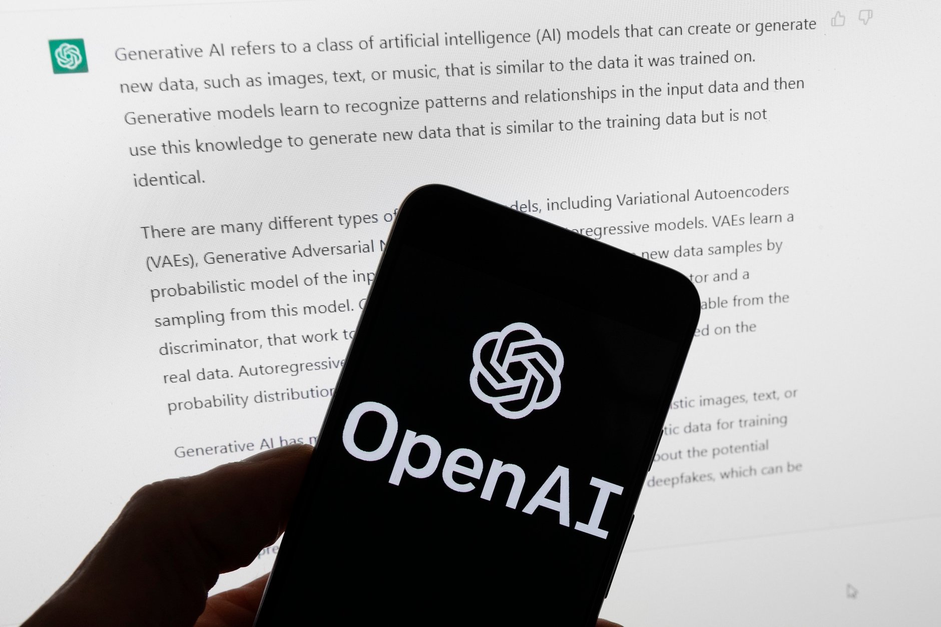The OpenAI logo is seen on a mobile phone in front of a computer screen displaying output from ChatGPT in Boston on March 21, 2023.