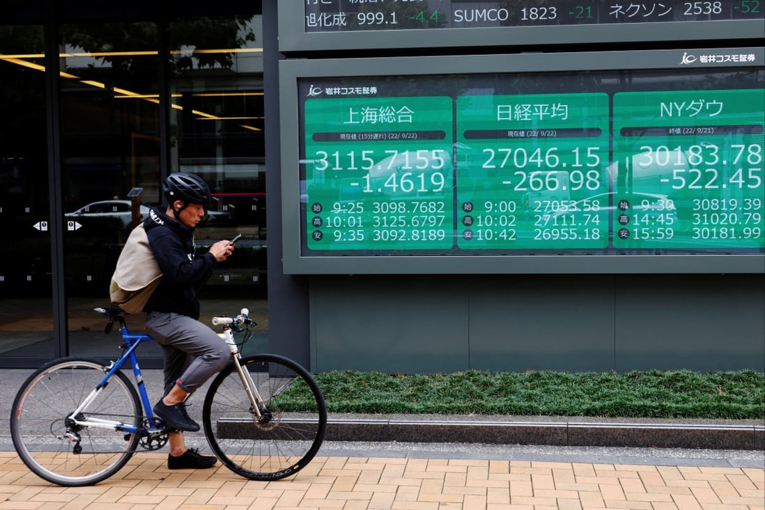A man on a bicycle stands in front of an electronic board showing Shanghai stock index and other major markets in Tokyo. Photo: Reuters
